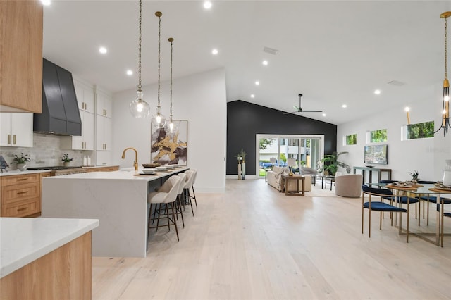 kitchen featuring custom exhaust hood, a spacious island, pendant lighting, white cabinetry, and lofted ceiling