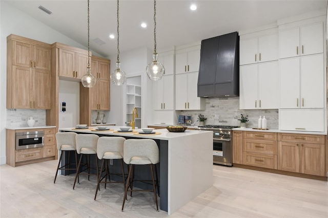 kitchen featuring a center island with sink, white cabinets, stainless steel appliances, and custom exhaust hood