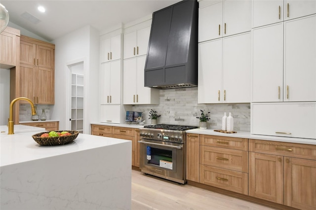 kitchen featuring custom range hood, vaulted ceiling, high end stainless steel range, light hardwood / wood-style floors, and white cabinetry