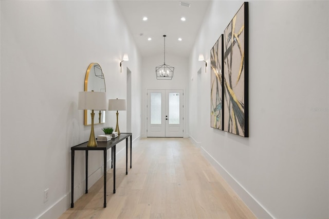 foyer with a chandelier, french doors, high vaulted ceiling, and light hardwood / wood-style flooring