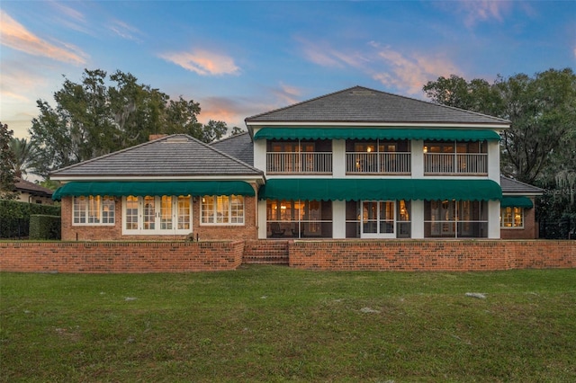 back house at dusk with a balcony and a yard