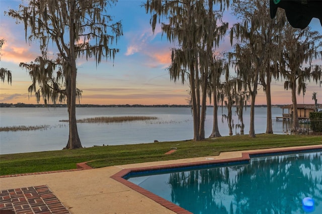 pool at dusk with a water view and a yard