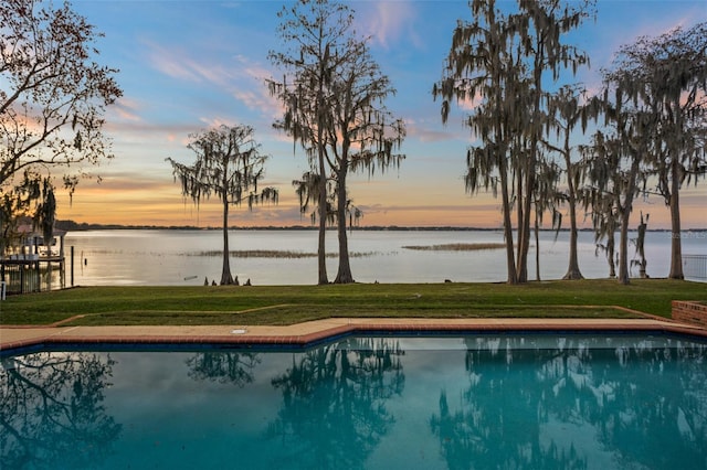 pool at dusk featuring a lawn and a water view