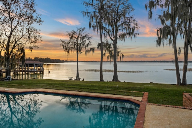 pool at dusk with a water view, a boat dock, and a yard