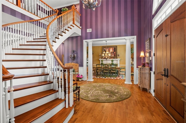 foyer entrance with ornate columns, hardwood / wood-style flooring, and a towering ceiling