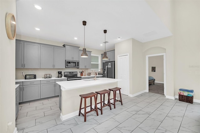 kitchen with decorative light fixtures, appliances with stainless steel finishes, a breakfast bar, sink, and an island with sink