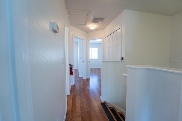 hall with baseboards, visible vents, dark wood finished floors, and an upstairs landing