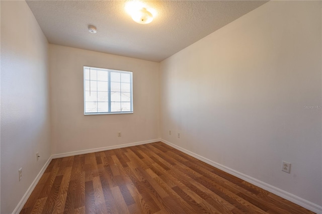 spare room with dark wood finished floors, a textured ceiling, and baseboards