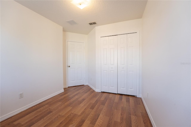 unfurnished bedroom with a closet, dark wood-style flooring, visible vents, and baseboards