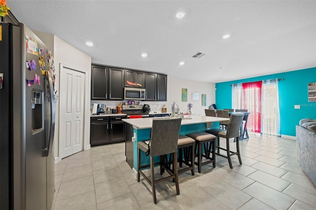 kitchen with a kitchen breakfast bar, a center island with sink, appliances with stainless steel finishes, and light tile floors