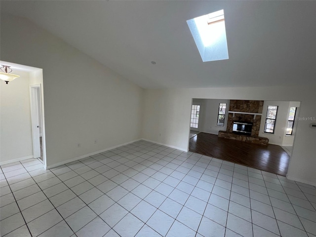 unfurnished living room with vaulted ceiling with skylight, a fireplace, and light tile patterned flooring