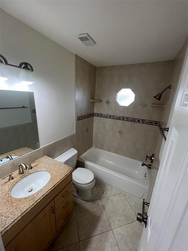 full bathroom featuring toilet, tile patterned flooring, tiled shower / bath, vanity, and tile walls