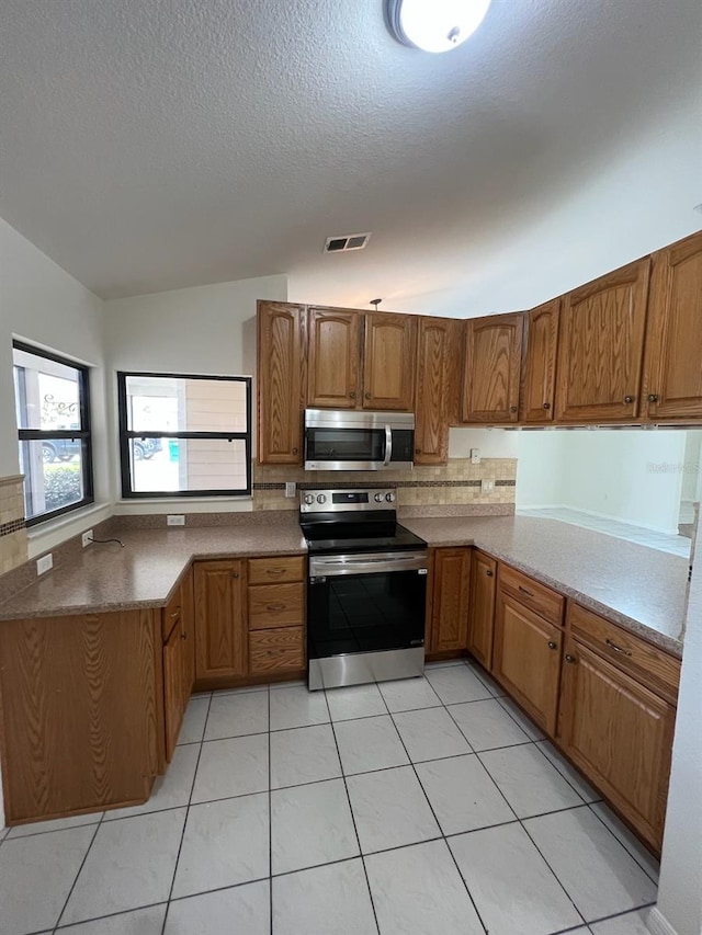 kitchen featuring light tile patterned floors, appliances with stainless steel finishes, lofted ceiling, kitchen peninsula, and a textured ceiling