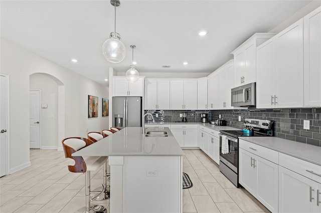 kitchen featuring an island with sink, pendant lighting, white cabinets, appliances with stainless steel finishes, and a breakfast bar