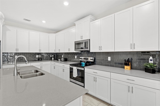 kitchen with stainless steel appliances, light tile floors, tasteful backsplash, white cabinets, and sink