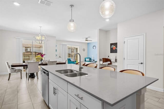 kitchen with light stone countertops, ceiling fan with notable chandelier, sink, an island with sink, and pendant lighting