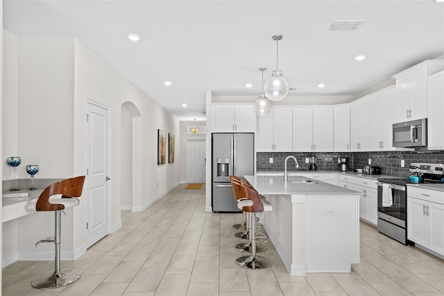 kitchen featuring hanging light fixtures, a breakfast bar, stainless steel appliances, a center island with sink, and white cabinets