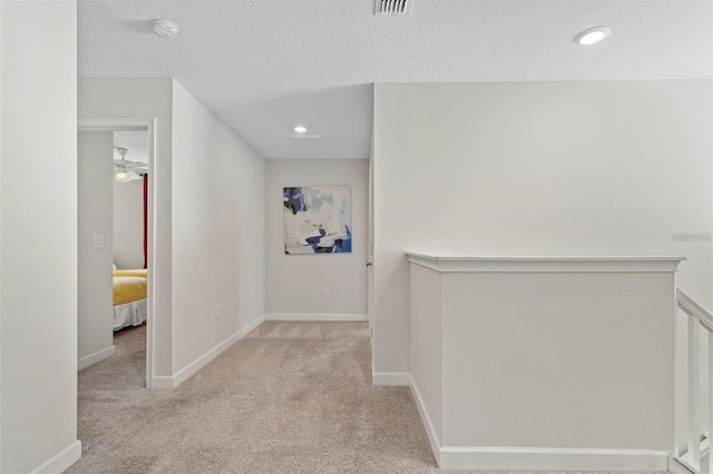 hall with light carpet and a textured ceiling