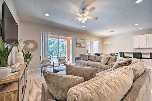 tiled living room featuring a textured ceiling and ceiling fan with notable chandelier