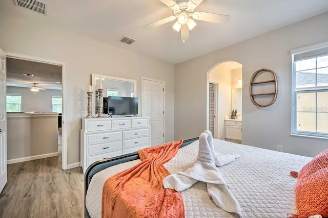 bedroom with ensuite bath, multiple windows, ceiling fan, and light wood-type flooring