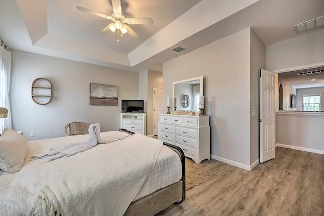 bedroom featuring ceiling fan, a tray ceiling, and light hardwood / wood-style flooring