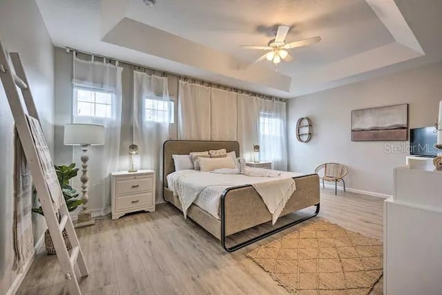 bedroom featuring a raised ceiling, ceiling fan, and light wood-type flooring