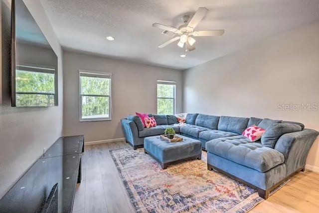 living room with a textured ceiling, ceiling fan, and light wood-type flooring