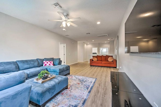 living room with light hardwood / wood-style floors, ceiling fan, and a textured ceiling