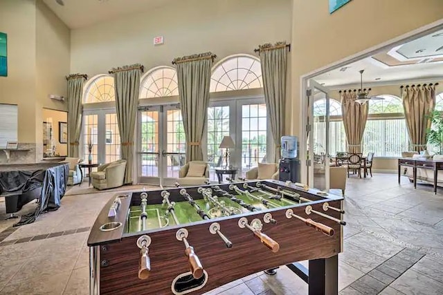 playroom featuring a notable chandelier, a towering ceiling, light tile floors, and french doors