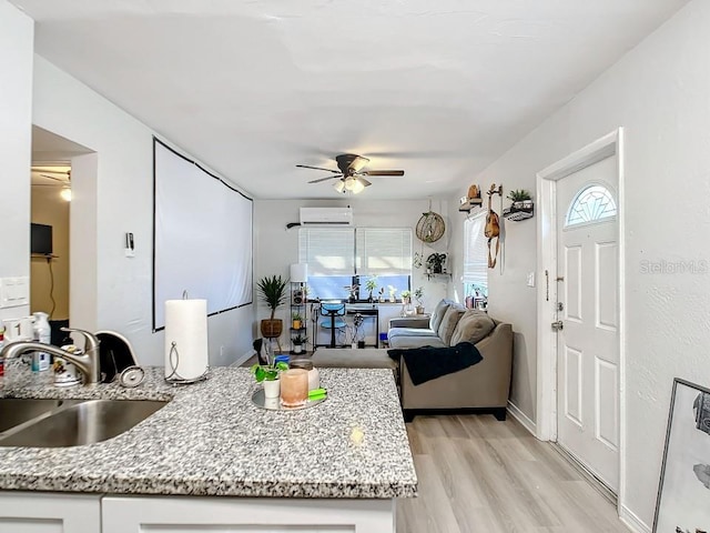 kitchen with sink, ceiling fan, an AC wall unit, light hardwood / wood-style flooring, and white cabinetry