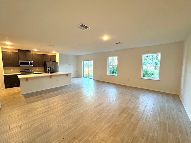 kitchen with sink, a breakfast bar area, light wood-type flooring, an island with sink, and stainless steel appliances