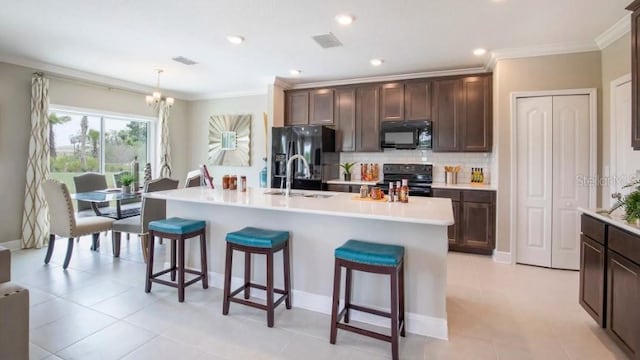 kitchen with hanging light fixtures, dark brown cabinetry, tasteful backsplash, black appliances, and an island with sink