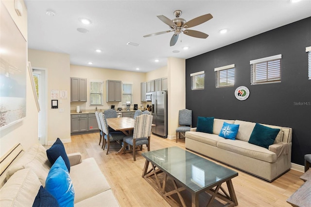 living room with a baseboard heating unit, ceiling fan, and light wood-type flooring