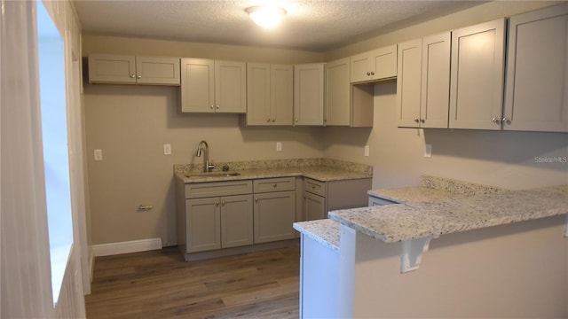 kitchen featuring a textured ceiling, a breakfast bar, kitchen peninsula, dark hardwood / wood-style floors, and sink