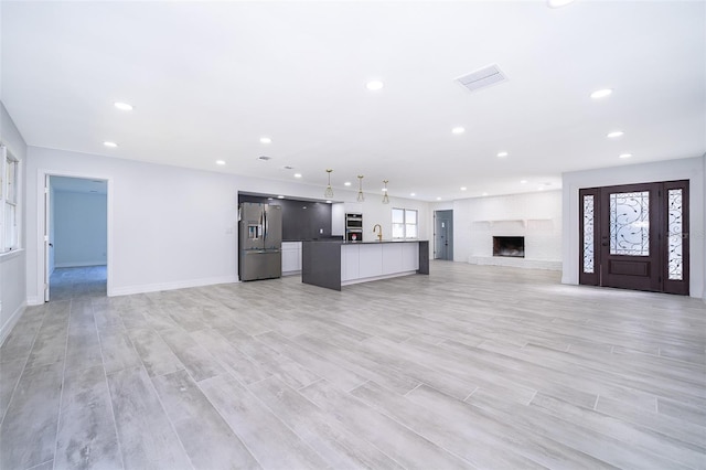 unfurnished living room featuring light wood-type flooring, sink, and a brick fireplace