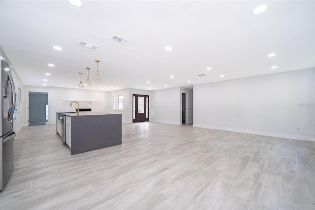 kitchen with hanging light fixtures, appliances with stainless steel finishes, sink, light hardwood / wood-style flooring, and a center island with sink