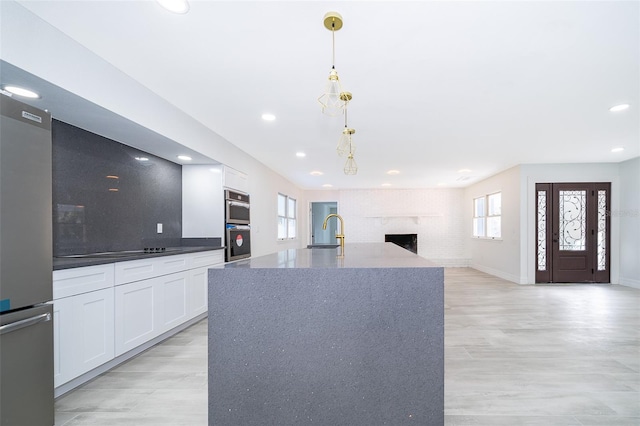 kitchen with decorative light fixtures, white cabinetry, sink, a brick fireplace, and light wood-type flooring