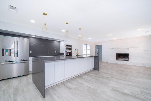 kitchen featuring a fireplace, brick wall, appliances with stainless steel finishes, white cabinets, and hanging light fixtures