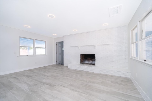 unfurnished living room with brick wall, light hardwood / wood-style flooring, and a fireplace