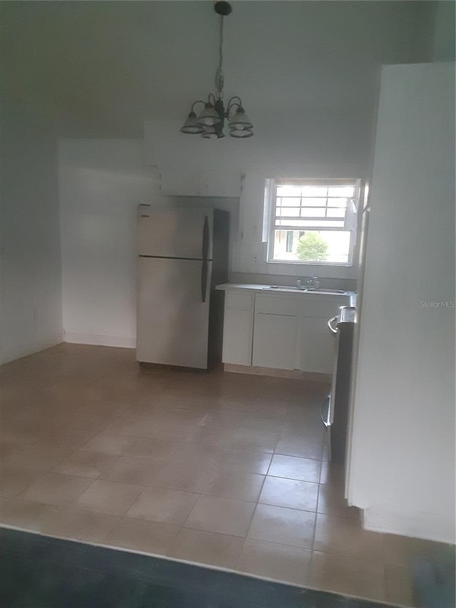 kitchen featuring light tile flooring, white cabinetry, an inviting chandelier, white fridge, and sink