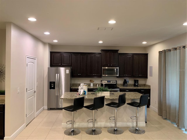 kitchen with light stone countertops, light tile patterned floors, a center island, stainless steel appliances, and a breakfast bar