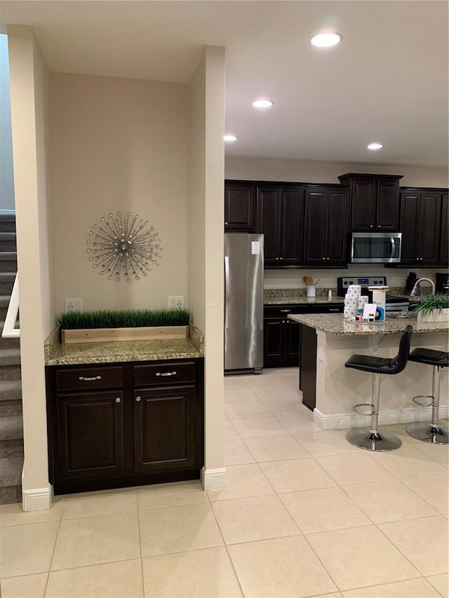 kitchen featuring light tile patterned floors, appliances with stainless steel finishes, light stone counters, kitchen peninsula, and a breakfast bar