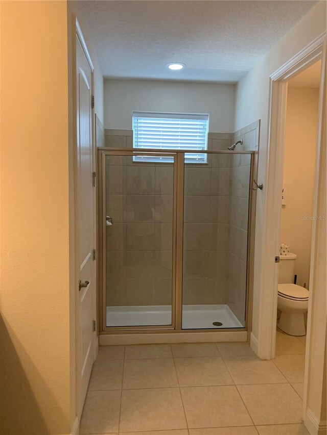 bathroom with walk in shower, toilet, and tile patterned flooring