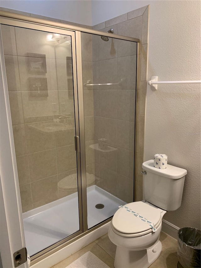 bathroom featuring toilet, a shower with shower door, and tile patterned flooring