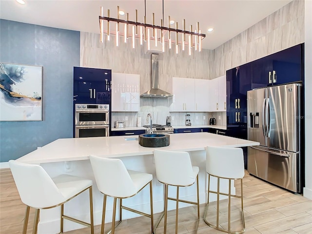 kitchen featuring a kitchen breakfast bar, stainless steel appliances, a center island with sink, wall chimney range hood, and pendant lighting