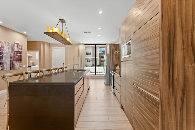 kitchen featuring an island with sink, pendant lighting, appliances with stainless steel finishes, and sink