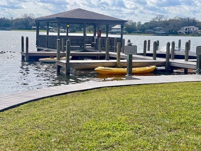 view of dock with a gazebo, a lawn, and a water view