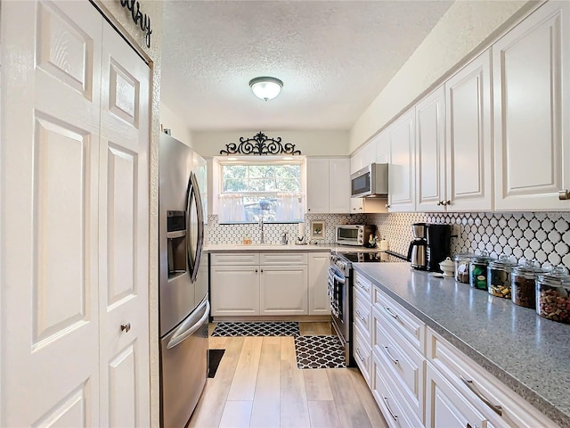 kitchen with appliances with stainless steel finishes, white cabinetry, decorative backsplash, light stone counters, and light wood-type flooring