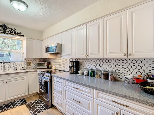 kitchen featuring light stone countertops, appliances with stainless steel finishes, white cabinets, and light hardwood / wood-style floors