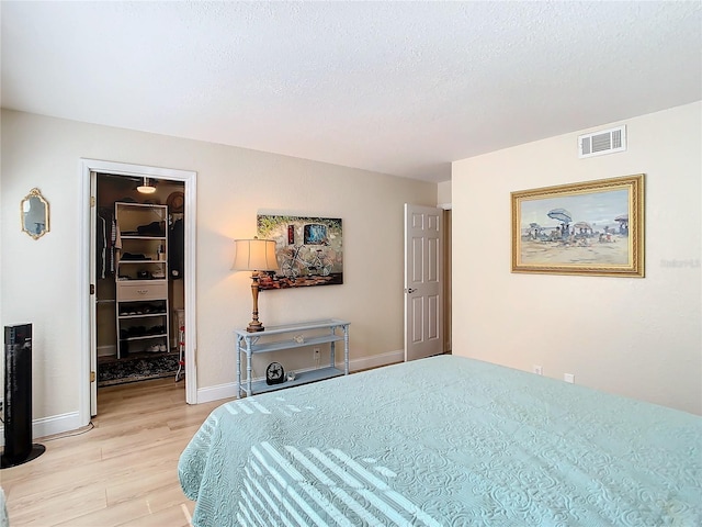 bedroom with a spacious closet, a textured ceiling, light wood-type flooring, and a closet